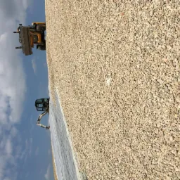 Żwirowe podłoże z widocznym w tle żółtym ładowaczem i koparką na tle błękitnego nieba.