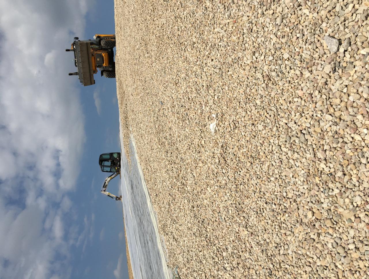 Żwirowe podłoże z widocznym w tle żółtym ładowaczem i koparką na tle błękitnego nieba.