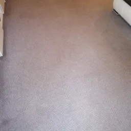 Szary dywan po czyszczeniu, widoczna struktura materiału, fragment białej sofy w prawym górnym rogu, ujęcie z góry.