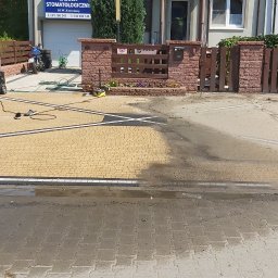 Usługi budowlano remontowe RYSZARD HĘCIAK - Żółta kostka brukowa na podjeździe częściowo umyta myjką ciśnieniową, widoczne różnice w kolorze między czystą a brudną powierzchnią, zarysowany wzór na kostce.