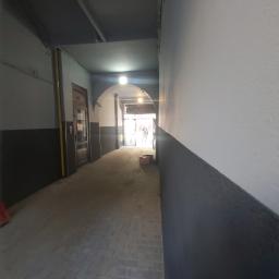 Usługi budowlano remontowe RYSZARD HĘCIAK - Korytarz wejściowy do budynku z szarą kostką brukową, ściany pomalowane w dwóch odcieniach szarości, widoczne drzwi wejściowe i łukowe przejście.