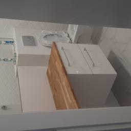 Usługi budowlano remontowe RYSZARD HĘCIAK - Nowoczesna łazienka w Grodzisku Wielkopolskim z białymi płytkami imitującymi marmur, zabudowaną toaletą z drewnianym blatem i minimalistyczną szafką pod umywalką.