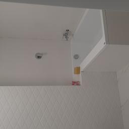 Usługi budowlano remontowe RYSZARD HĘCIAK - Nowoczesna łazienka z białą armaturą, kabiną prysznicową typu walk-in i geometrycznymi płytkami ściennymi, widok na baterię i deszczownicę.