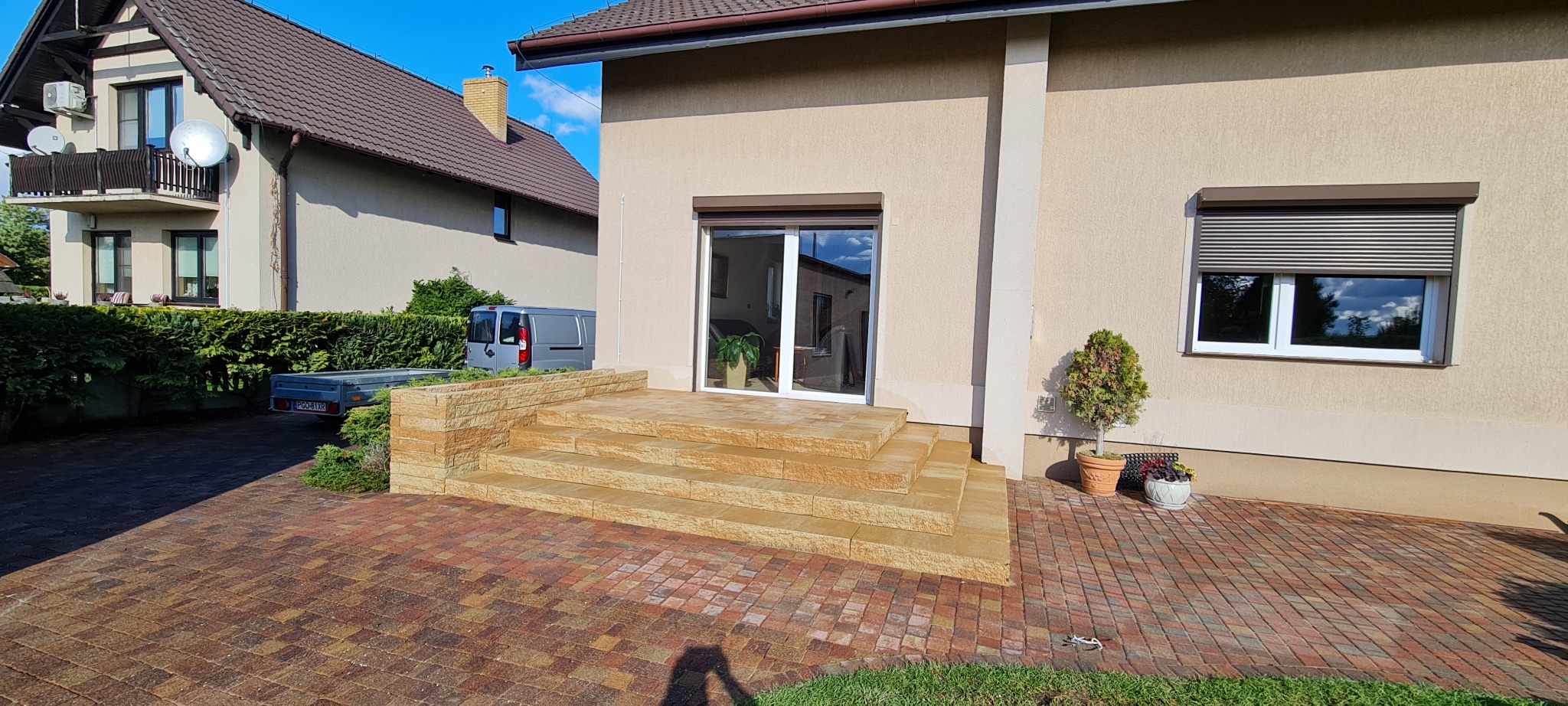 Zewnętrzne schody wejściowe z piaskowca prowadzące do domu z przesuwanymi drzwiami, otoczone kostką brukową w odcieniach czerwieni i brązu.