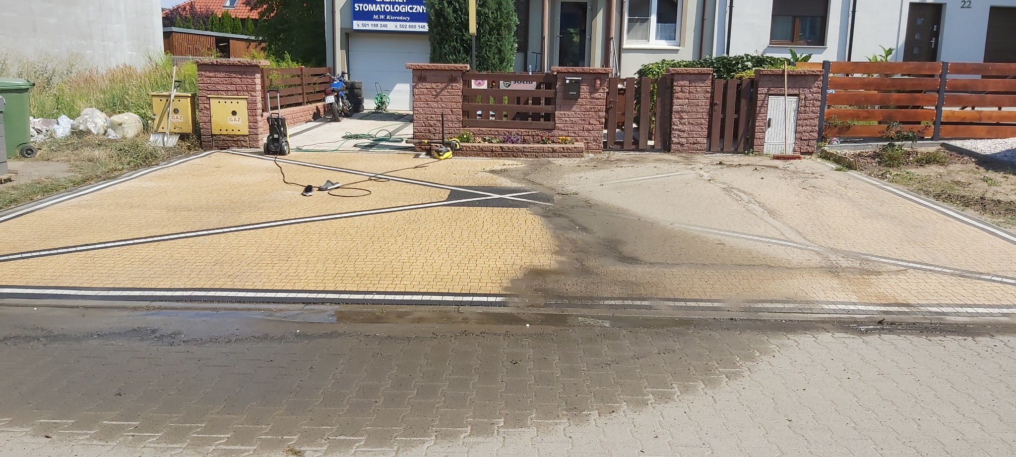 Żółta kostka brukowa na podjeździe częściowo umyta myjką ciśnieniową, widoczne różnice w kolorze między czystą a brudną powierzchnią, zarysowany wzór na kostce.