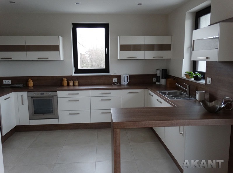 Jasna kuchnia w kształcie litery U z białymi szafkami i drewnianymi blatami, wyposażona w sprzęt AGD i dekoracje, widok na zewnątrz przez okno.