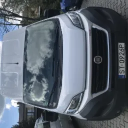 Biały samochód dostawczy Fiat Ducato z polską tablicą rejestracyjną ST 0926P, zaparkowany na brukowanej powierzchni, z widocznym odbiciem chmur na przedniej szybie.