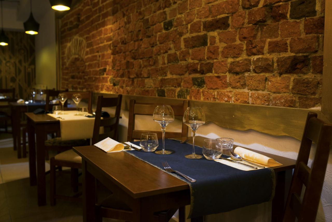 Nakryty stół w restauracji z ceglaną ścianą w tle, eleganckie szkło i ciemnoniebieski bieżnik.