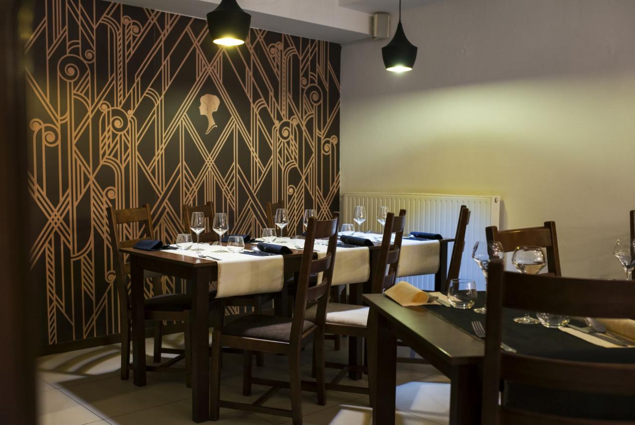 Elegancko nakryty stół w restauracji z art deco tapetą i minimalistycznymi lampami wiszącymi.