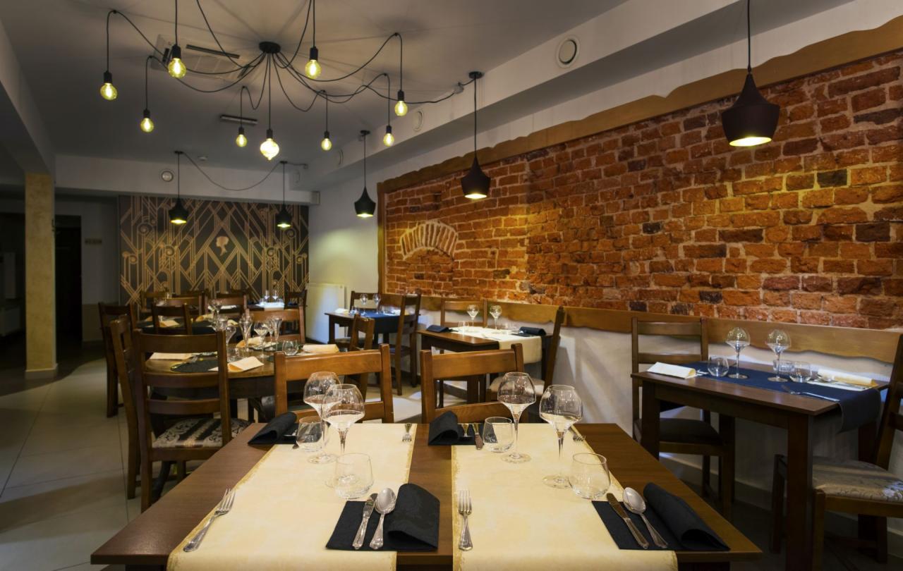 Elegancko nakryte stoły w restauracji z ceglaną ścianą w tle i designerskim oświetleniem z żarówkami Edisona.