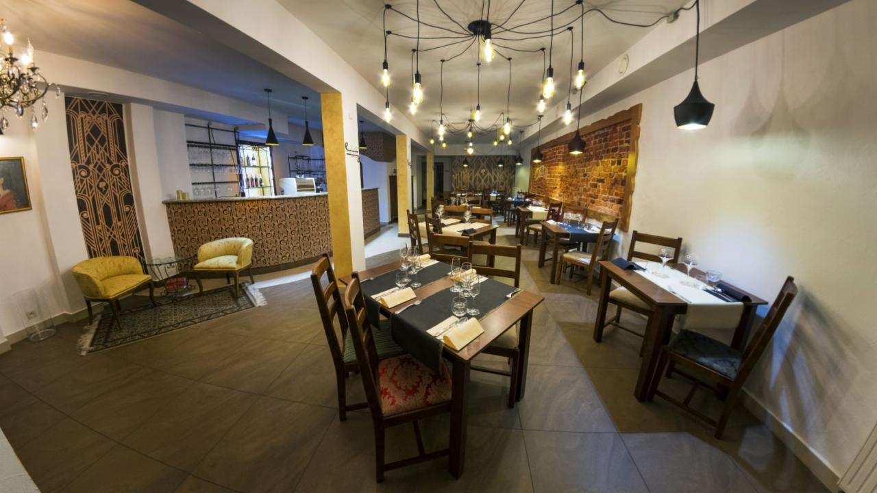 Wnętrze restauracji z nakrytymi stolami, dekoracyjną ścianą z cegły, nowoczesnymi lampami wiszącymi i barem w tle.
