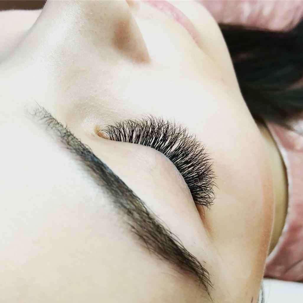 Detal portretu kobiety z profesjonalnie przedłużonymi, gęstymi rzęsami w odcieniu głębokiej czerni, widoczne subtelne cieniowanie na powiece.