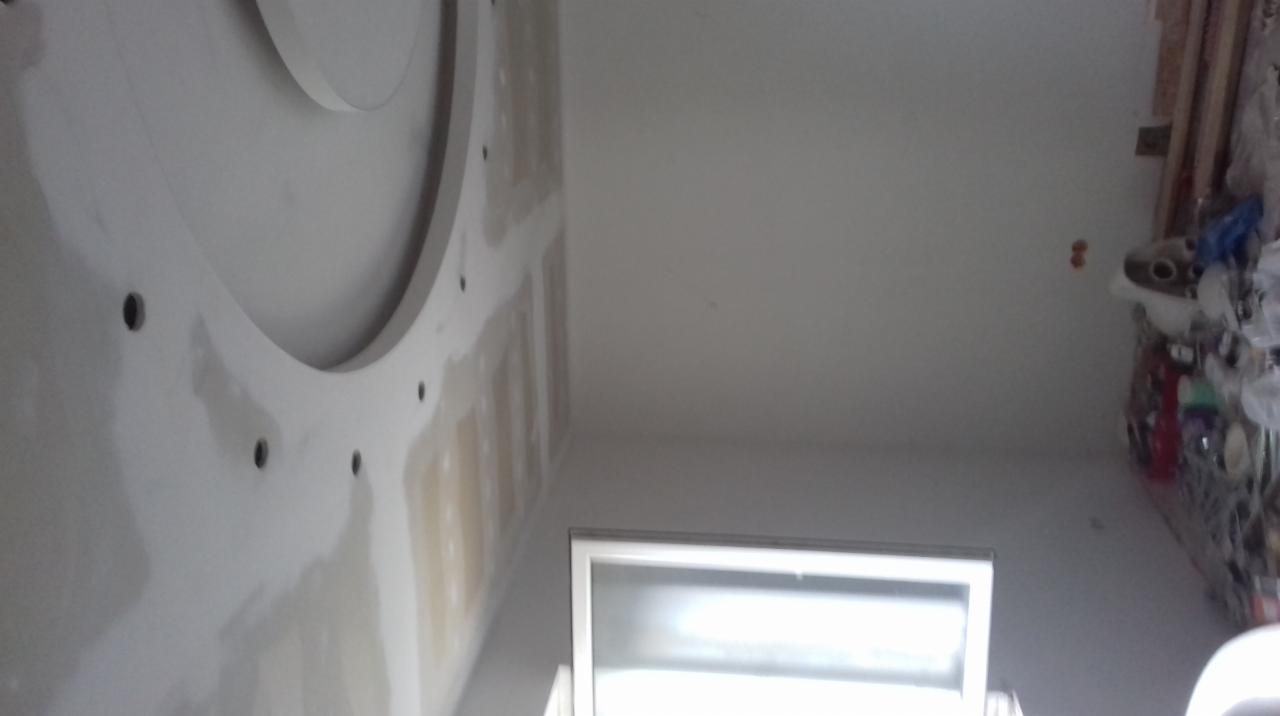 Sufit z zamontowaną dekoracyjną konstrukcją gipsowo-kartonową w trakcie szpachlowania, widoczne otwory montażowe i niedoskonałości powierzchni przed malowaniem, okno w dolnej części kadru.