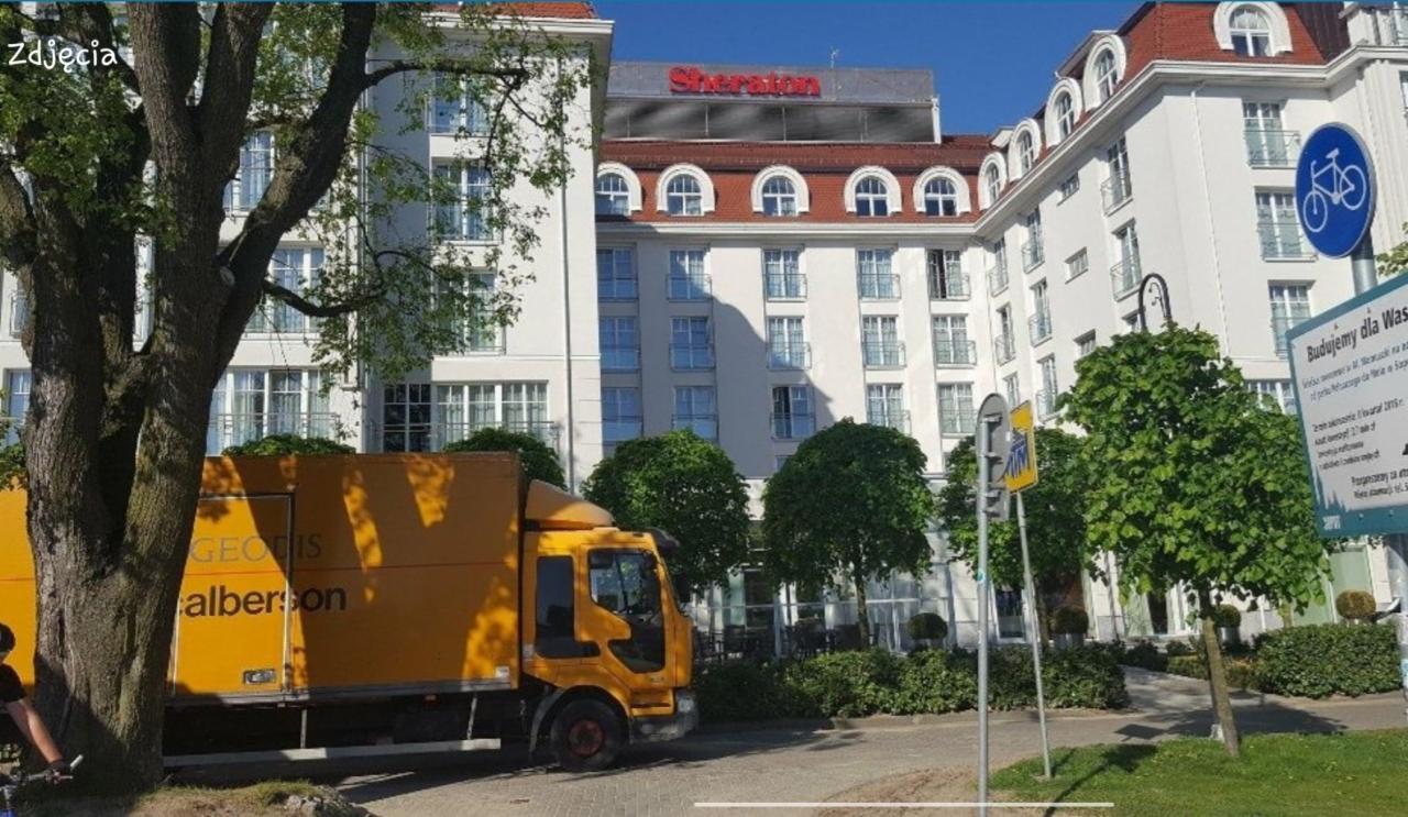 Żółta ciężarówka firmy GEODIS alberson zaparkowana przed hotelem Sheraton z niebieskim znakiem ścieżki rowerowej w Sopocie.