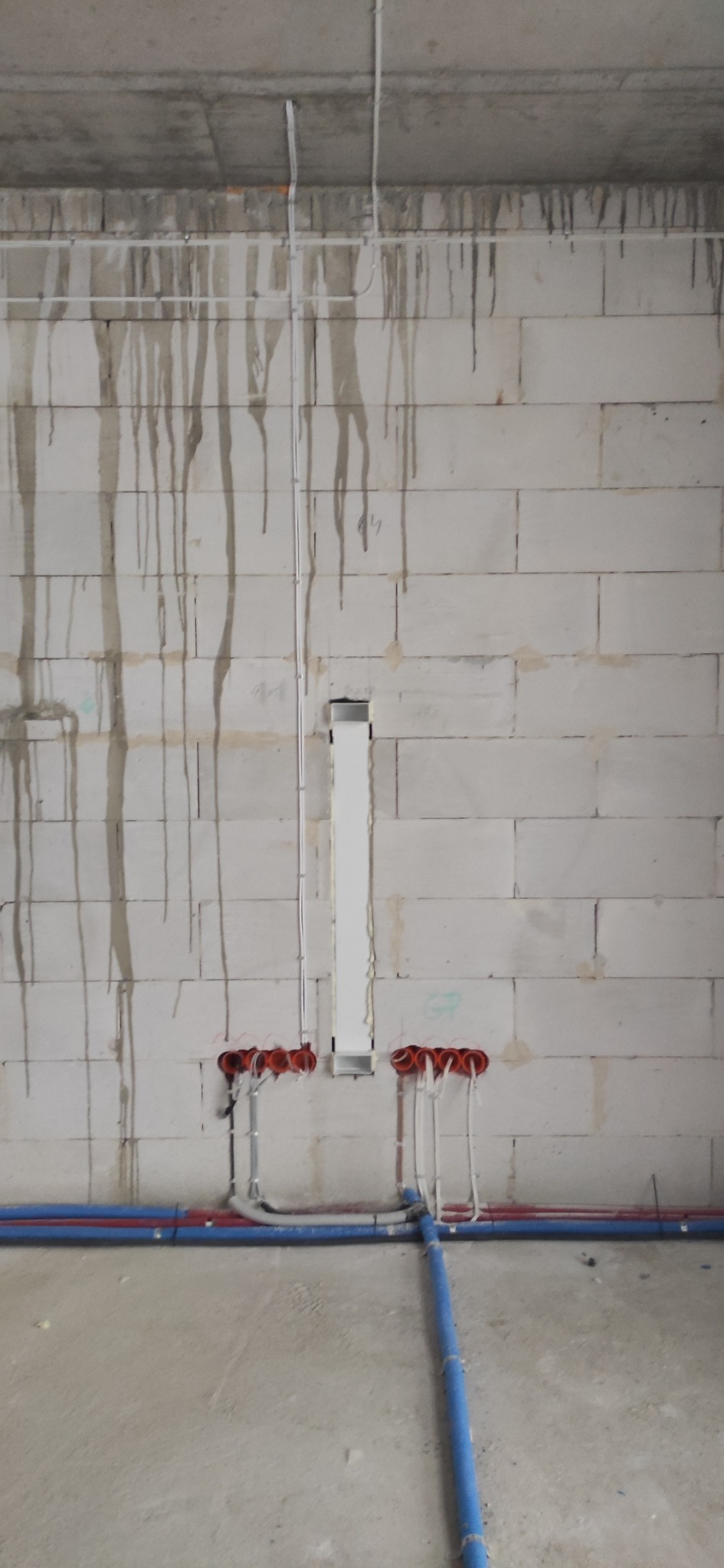 Surowa ściana z betonu komórkowego z widocznymi śladami po zalaniu, instalacja elektryczna w trakcie montażu: puszki podtynkowe z przewodami i pionowy kanał kablowy, oraz instalacja wodna...