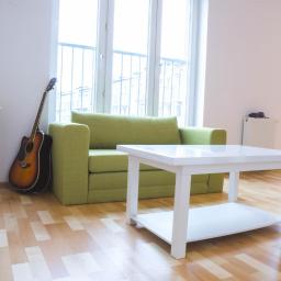 Jelongraphy - Jasny pokój dzienny z zieloną sofą, białym stolikiem kawowym, drewnianą podłogą i gitarą opartą o ścianę obok okna.