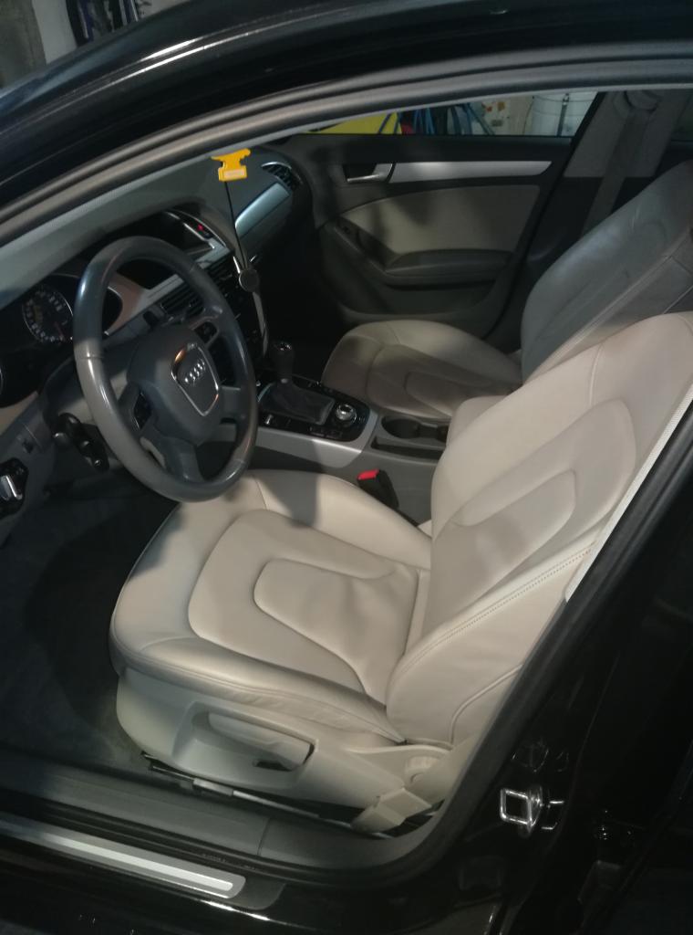 Wnętrze czarnego samochodu Audi z jasną skórzaną tapicerką foteli, widoczne z otwartych drzwi kierowcy, z żółtą zawieszką zapachową na lusterku.