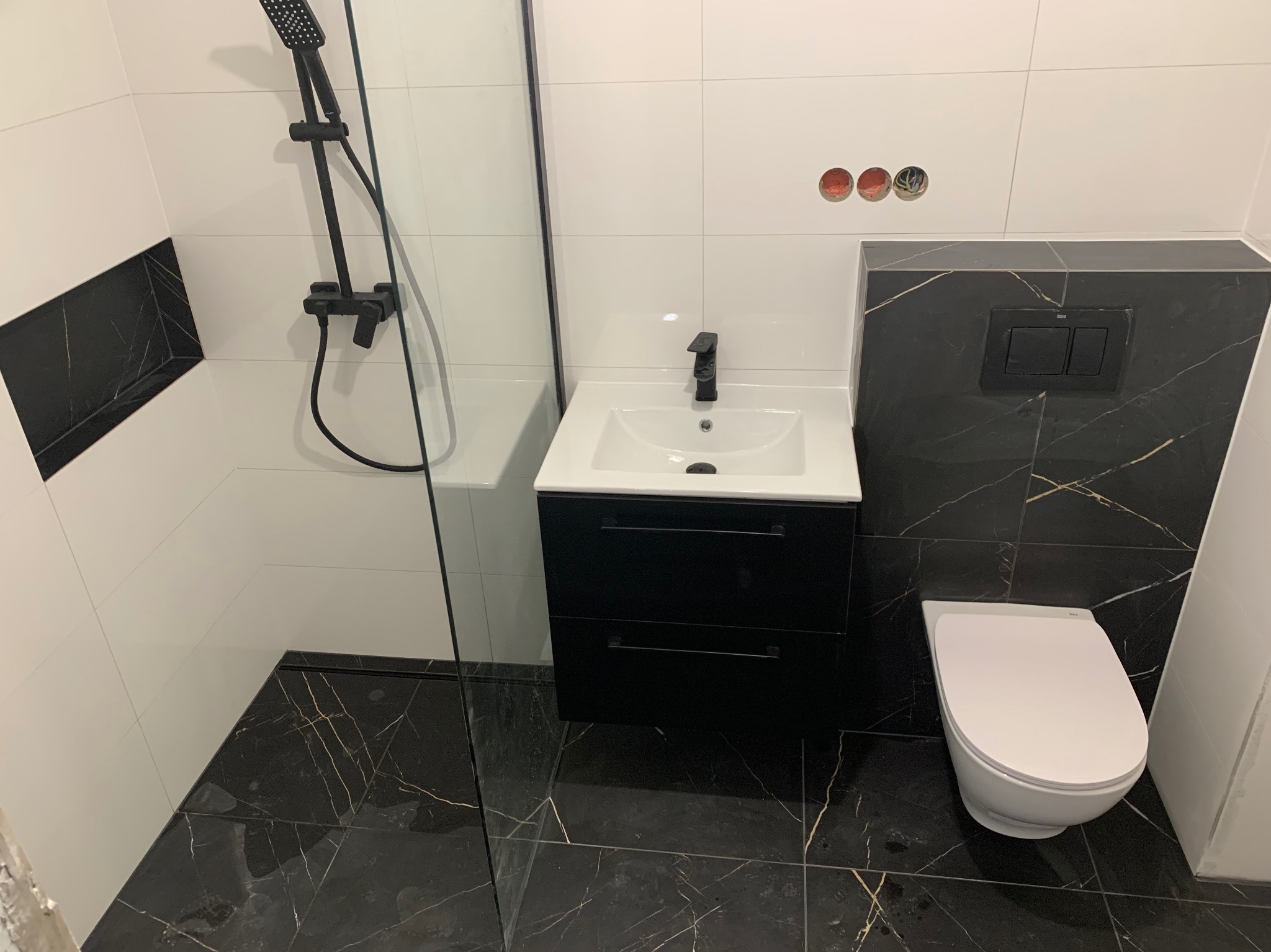 Nowoczesna łazienka w Warszawie z czarno-białymi płytkami imitującymi marmur, czarną armaturą i kabiną prysznicową typu walk-in.