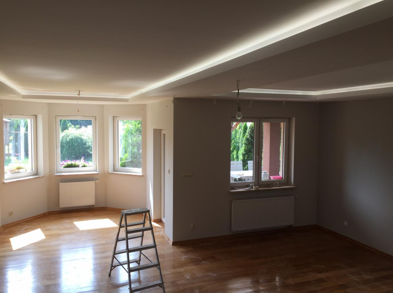 Jasne wnętrze po malowaniu ścian na szaro, z drewnianą podłogą, schodami malarskimi i oświetleniem sufitowym LED.