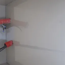 Aplikacja samopoziomującego szarego podkładu podłogowego przy użyciu węża i pompy w narożniku pomieszczenia.