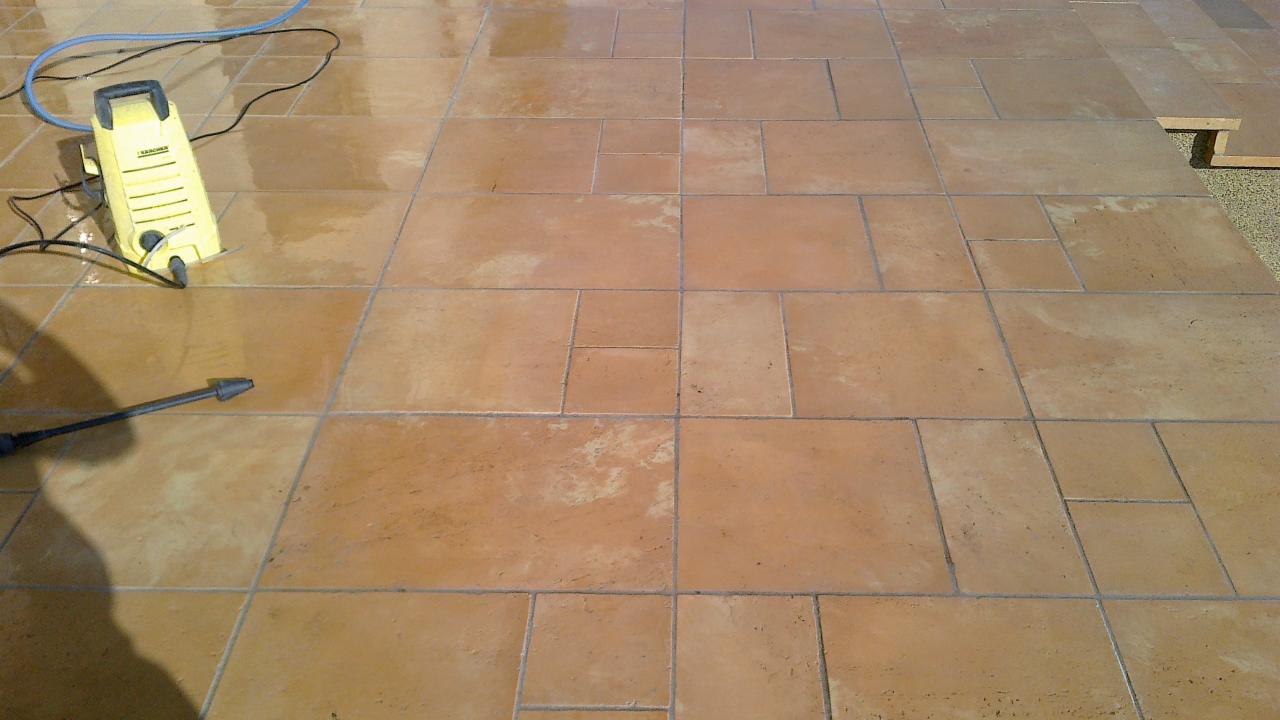 Czyszczenie kostki brukowej z użyciem myjki ciśnieniowej Kärcher; widoczne mokre, brązowe płytki po umyciu.