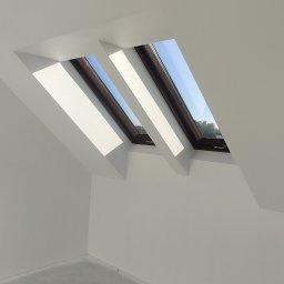 Jackowicz Tomasz - Białe wnętrze poddasza z trzema oknami dachowymi, widok na niebo. Ściany i sufit świeżo pomalowane, podłoga przygotowana do dalszych prac wykończeniowych.