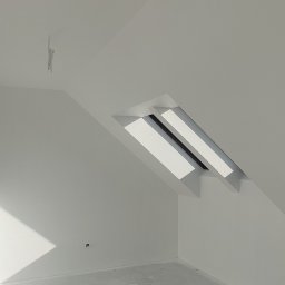 Jackowicz Tomasz - Poddasze po remoncie: świeżo pomalowane ściany na biało, okno dachowe w skosie, widoczne przewody elektryczne. Minimalistyczny wystrój, surowy beton na podłodze.