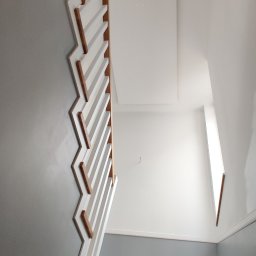 Jackowicz Tomasz - Klatka schodowa po remoncie: szare ściany, białe schody z drewnianymi elementami, widok z góry. Nowoczesne wykończenie wnętrza, świeżo pomalowane ściany.