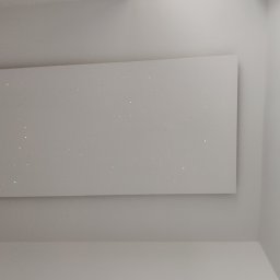 Jackowicz Tomasz - Biała ściana z zamontowaną płytą z efektem gwiazd, widoczny fragment sufitu i ściany bocznej, oświetlenie punktowe po lewej stronie.