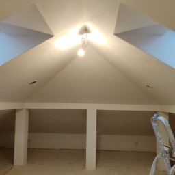 Jackowicz Tomasz - Poddasze po remoncie z oknami dachowymi i świeżo pomalowanymi ścianami na biało. Widoczna drabina malarska i metalowy profil przy ścianie.