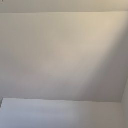 Jackowicz Tomasz - Białe, świeżo pomalowane poddasze ze skosami i oknem dachowym. Widoczne gładkie powierzchnie ścian i sufitu, bez widocznych łączeń. Minimalistyczny design.