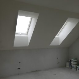 Jackowicz Tomasz - Poddasze po szpachlowaniu, z dwoma oknami dachowymi i widocznymi puszkami elektrycznymi w ścianie. Na podłodze ślady po pracach, w rogu widoczne wiadra z masą szpachlową.