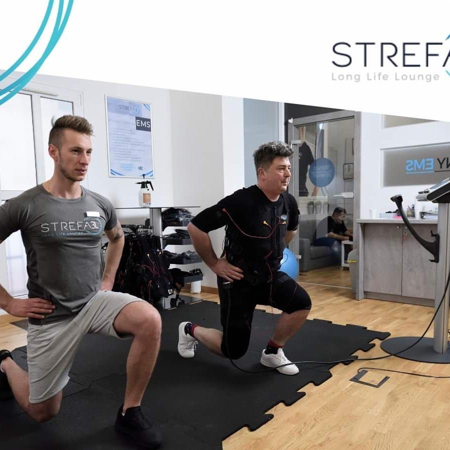 Trening EMS: Mężczyźni wykonują przysiady w specjalnych kombinezonach do elektrostymulacji, w tle widoczne logo 'STREFA Long Life Lounge'.