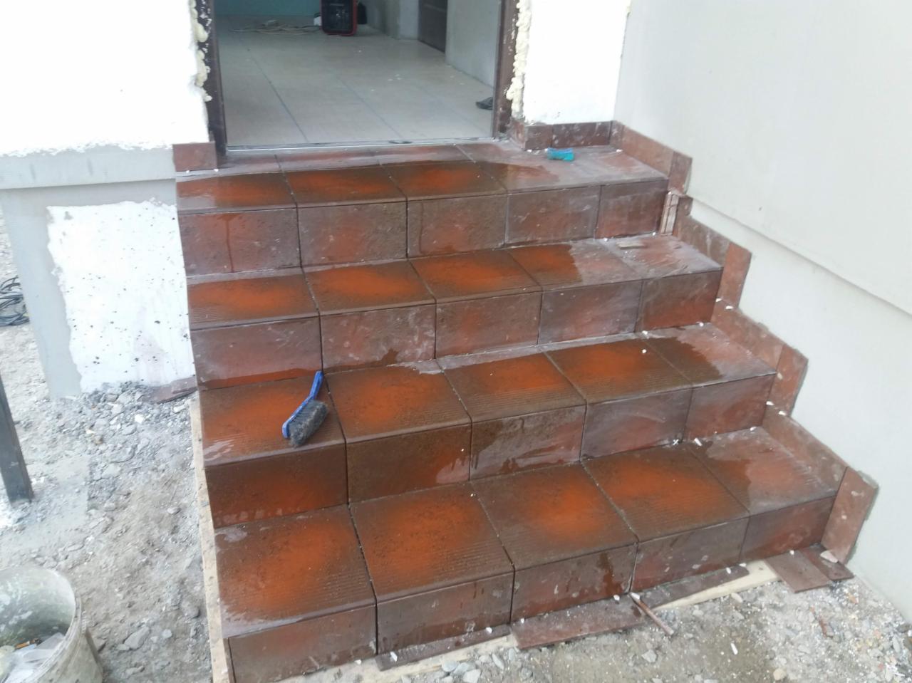 Wykończone płytkami schody wejściowe do budynku, widoczna fuga, szczotka do czyszczenia i resztki zaprawy.