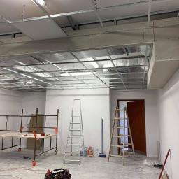 WALASEK-BUD - Montaż sufitu podwieszanego w biurze, widoczne rusztowanie, drabiny i narzędzia, surowy stan wykończenia.