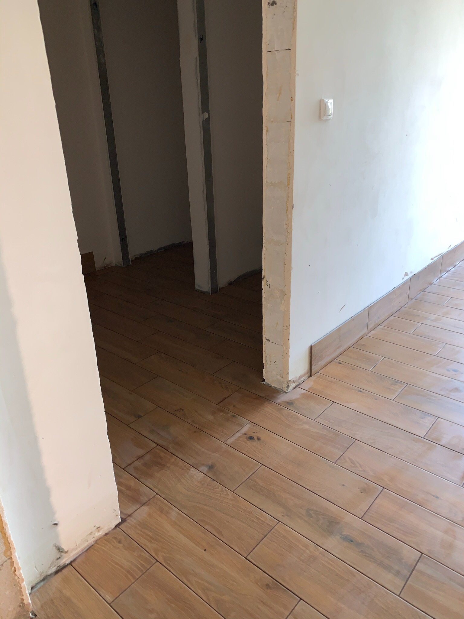 Korytarz w trakcie remontu z ułożoną drewnopodobną glazurą podłogową, widoczne niedokończone ściany i ościeżnice.