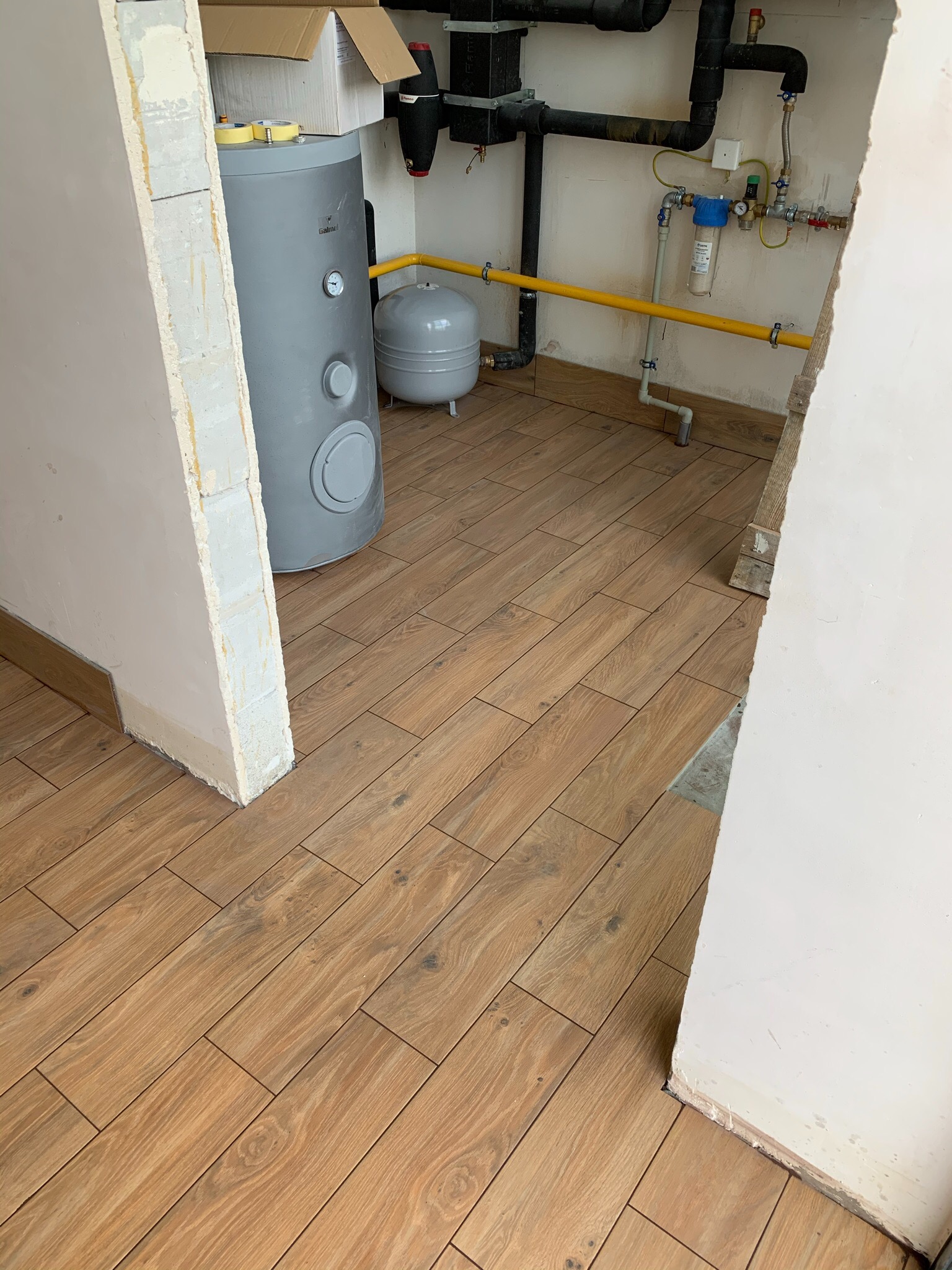 Ułożona podłoga z płytek imitujących drewno w remontowanej łazience, widoczne instalacje wodne i grzewcze oraz bojler.