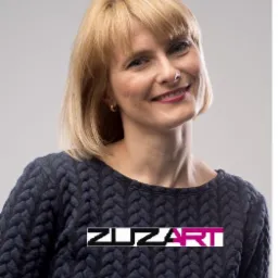 Portret uśmiechniętej kobiety z krótkimi blond włosami, w ciemnoniebieskim swetrze z warkoczowym wzorem, na neutralnym tle. Na swetrze widoczne logo firmy ZUZART. Zdjęcie wykonane w Warszawie.