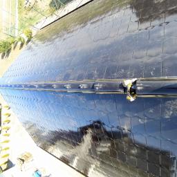 Dach Pol Zieliński - Błyszczący, czarny dach pokryty dachówką karpiówką w trakcie montażu, widok z góry, z widoczną częścią nowej rynny i fragmentem buta dekarza.