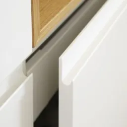 Detal minimalistycznej, białej szafki z drewnianym elementem, widok z bliska na uchwyty i krawędzie frontów.