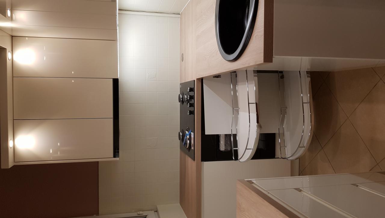 Nowoczesna kuchnia z białymi, lakierowanymi frontami szafek, czarnym zlewozmywakiem i narożną szafką z półkami obrotowymi.