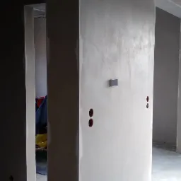 Świeżo położona gładź na ścianie z widocznymi otworami na puszki elektryczne i puszkami wentylacyjnymi, surowy stan wykończenia wnętrza.