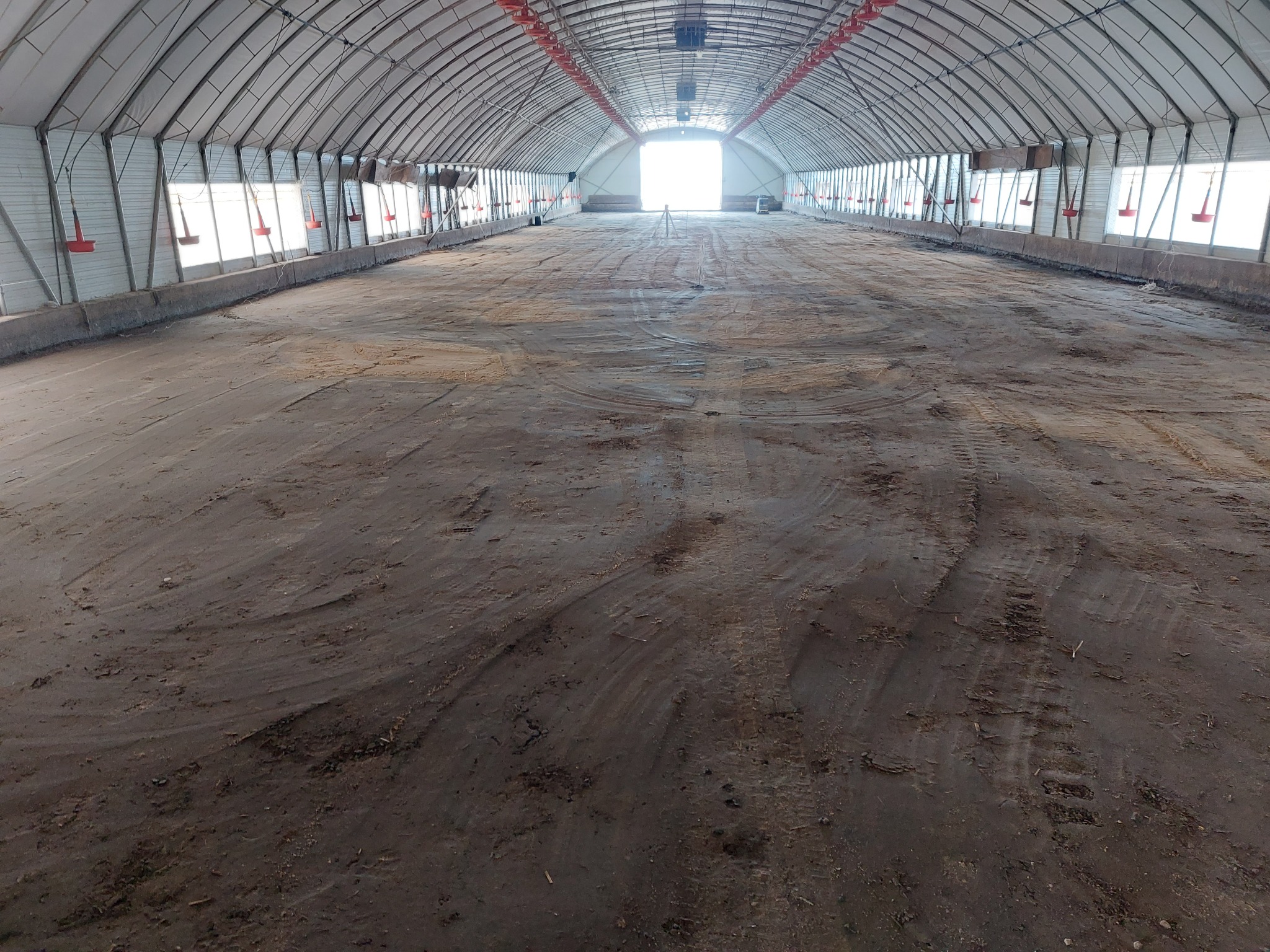 Przygotowanie podłoża w hali z metalową konstrukcją i oświetleniem, widoczne ślady opon. W tle jasne światło wpadające przez otwór.