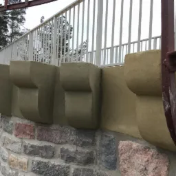 Kamienny mur z odnowionymi wspornikami pod balustradą, widoczny fragment metalowej konstrukcji schodów.