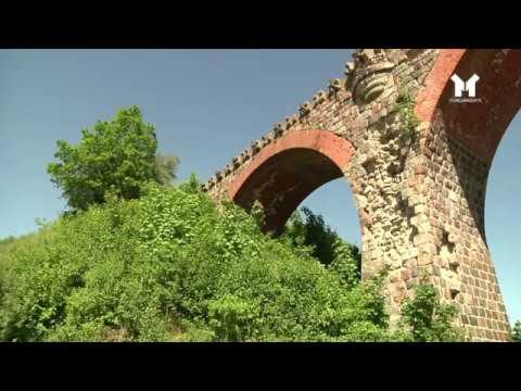 Stary, ceglany wiadukt porośnięty roślinnością, widziany z dołu pod kątem.