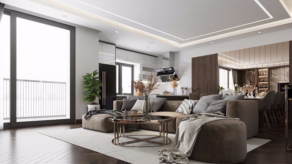 Wnętrze apartamentu: brązowa sofa narożna z szarymi poduszkami, okrągły stolik kawowy ze szklanym blatem, parkiet w jodełkę, duże okno balkonowe z widokiem na zewnątrz, otwarta kuchnia z białymi...