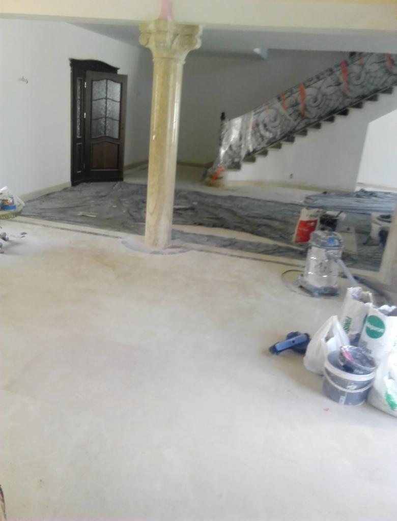 Wnętrze w trakcie remontu: podłoga przygotowana do położenia nawierzchni, kolumna w stylu klasycznym z zabezpieczeniem na górze, drzwi z szybą i schody zabezpieczone folią ochronną, widoczne...