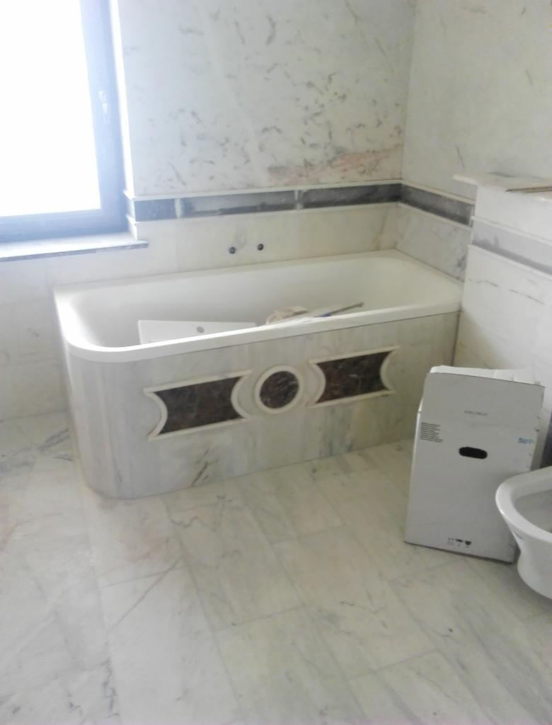 Wanna obudowana marmurem z dekoracyjnymi elementami, widoczna w trakcie remontu łazienki, z pudełkiem po ceramice sanitarną obok.