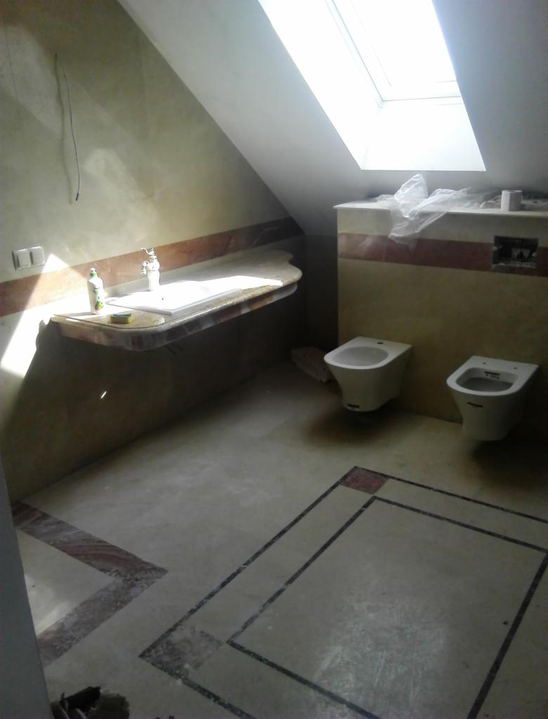 Remontowana łazienka na poddaszu z marmurowym blatem umywalki, bidetem i sedesem, widoczne ślady po remoncie i niezabezpieczone otwory w ścianie.