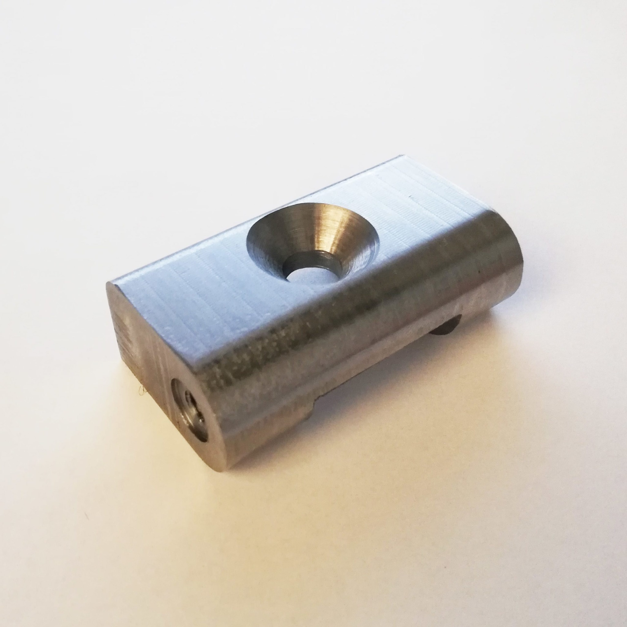 Metalowy element z otworem stożkowym i gwintowanym otworem bocznym, obrobiony na tokarce, leżący na jasnym tle.